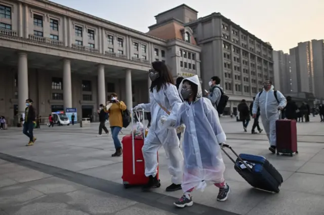 Passengers in protective suits towing luggage