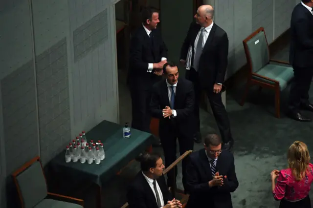 Australian MPs rub their hands after using hand sanitiser at the entrance of the chamber