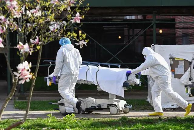 Medical personnel transport the body of a deceased patient from a refrigerated truck to Kingsbrook Jewish Medical Center on 8 April, 2020 in Brooklyn, New York