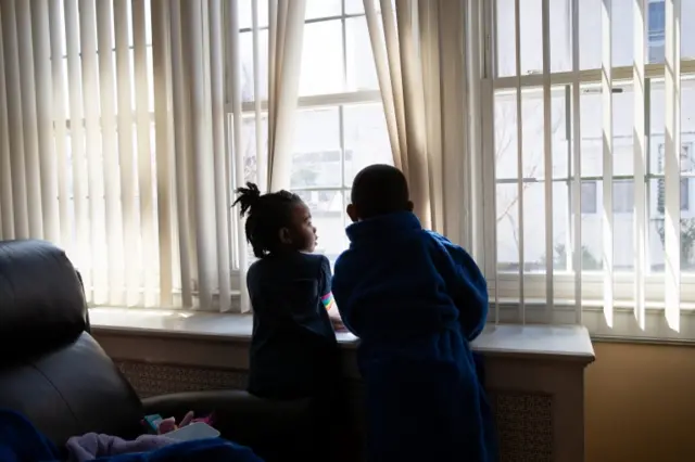 A brother and sister look out the window in New York after their parents lost their jobs because of the coronavirus pandemic