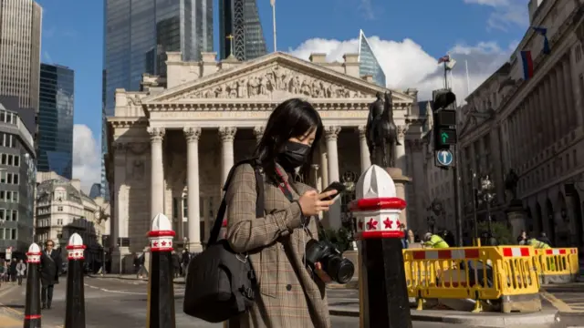 A woman wearing a mask walks past the Bank of England HQ