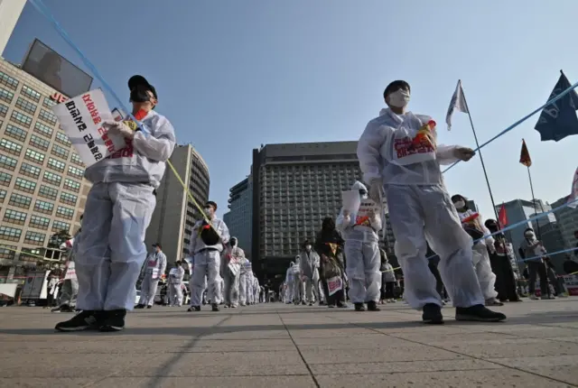 South Korean workers wearing protective clothing hold ropes to keep their distance from one another during a May Day rally in Seoul