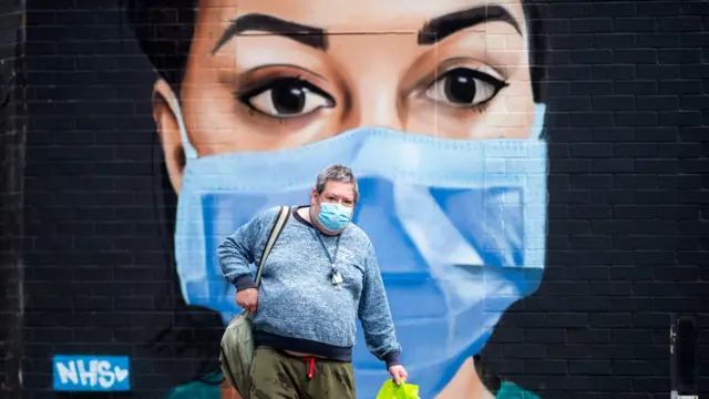 Man wearing a face mask walks past a mural in London