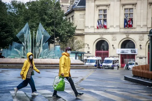 A couple wearing yellow jackets and protective face masks walk at the Gambetta Place in Paris