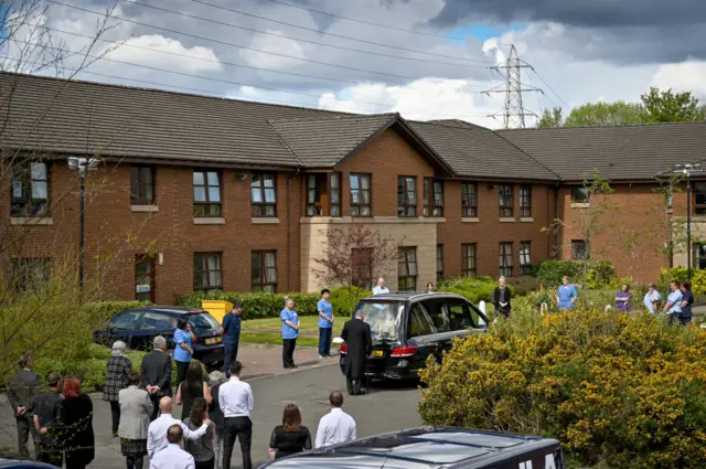 Staff and family stand beside a hearse carrying a former resident of a care home in Paisley