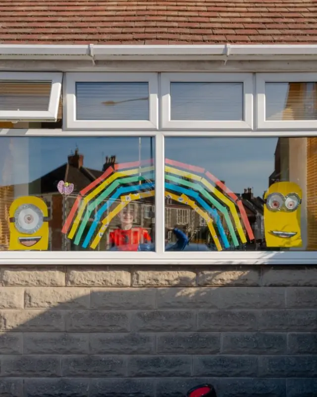 Finn stands in his window covered with a rainbow and two cartoon minions