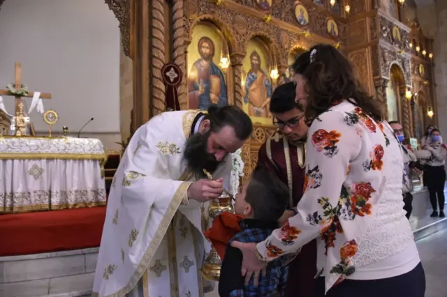 A child takes communion from a Roman Orthodox priest following the Sunday mass at the Saint Elias church Aleppo, Syria on May 10, 2020