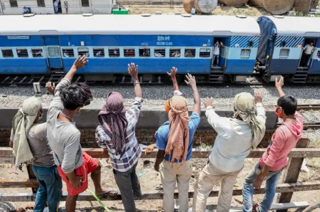 Labourers standing on a roadside wave to migrant workers and families sitting in a special train from Amritsar to Barauni of Bihar state as they go back to their hometowns May 10, 2020 after the government eased a nationwide lockdown