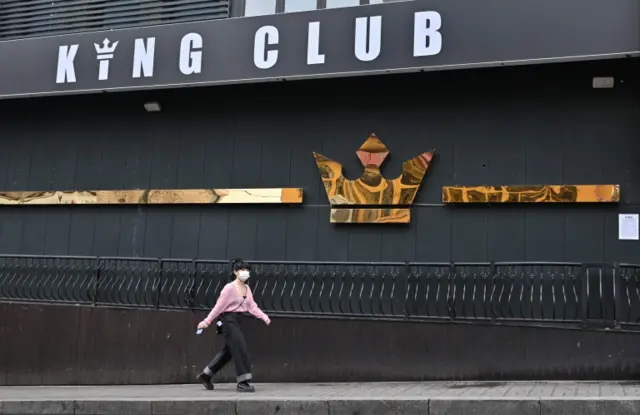 A woman wearing a face mask walks past a night club in Seoul