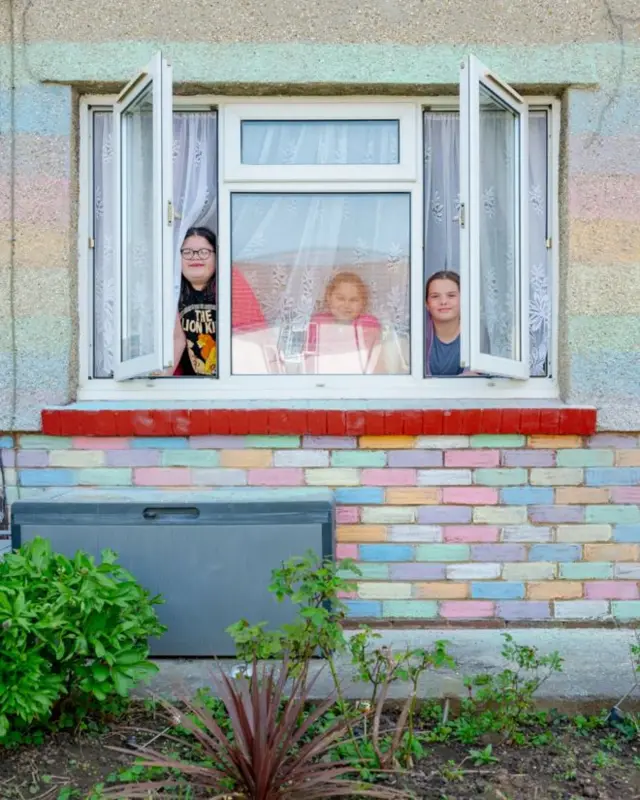 Millie, Sophia and Maddie look out the window of their rainbow-chalked house