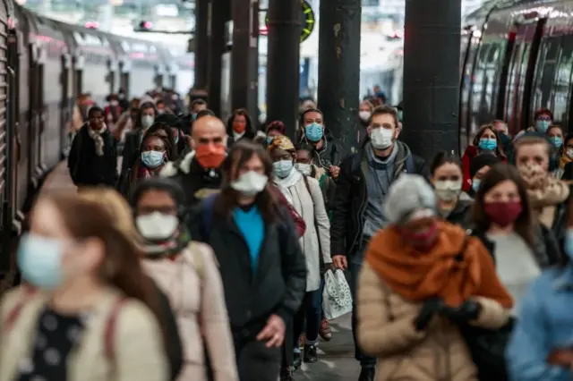 Commuters wearing face masks walk at the Saint Lazare railway station in Paris