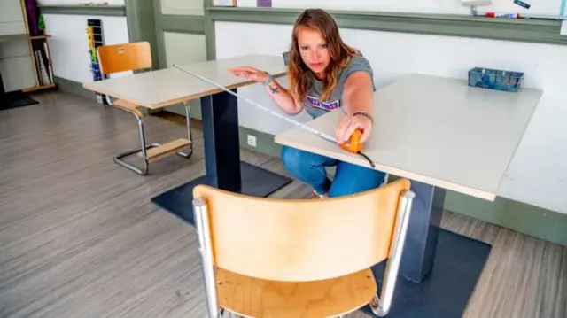 A teacher with a measuring tape between desks