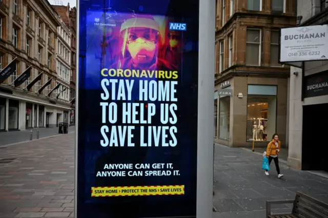 Members of the public walk past a sign asking people to stay at home during the Coronavirus crisis on 31 March 2020 in Glasgow, Scotland