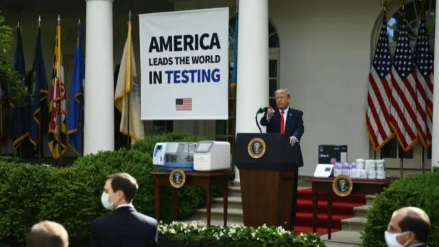 Trump speaking in front of a banner that says "America leads the world in testing"