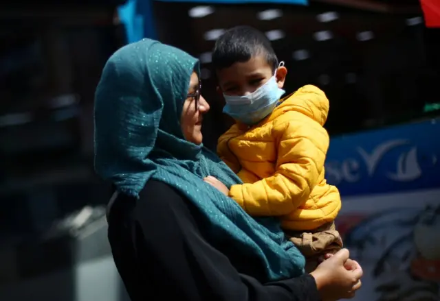 Woman holding a child who is wearing a mask in south London