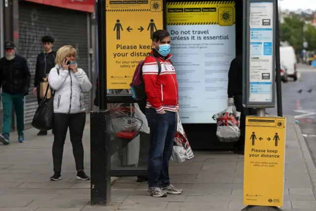 A man wearing a protective face mask waits at a bus stop in Camden, central London, on 11 May 2020