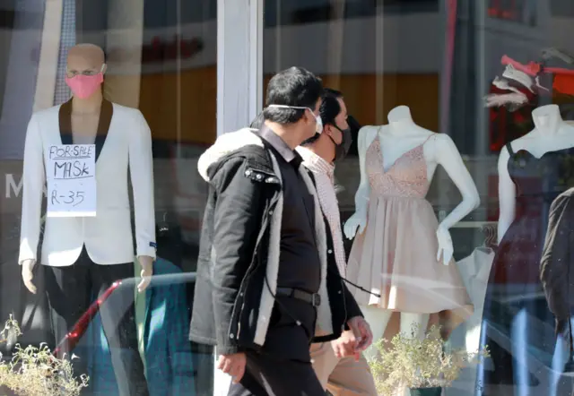 People with masks on stand in front of a shop window in Sea Point on May 06, 2020 in Cape Town, South Africa