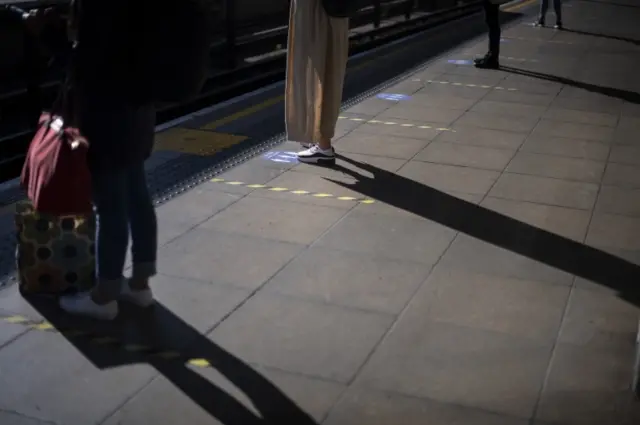 Passengers standing between markings at Canning Town station in London on Tuesday