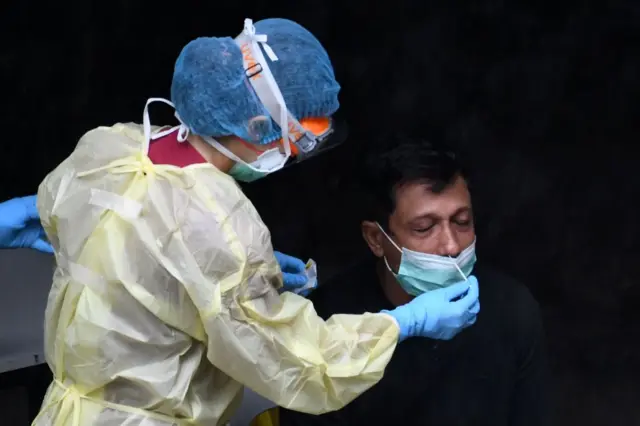 A healthcare worker dressed in personal protective equipment collects a nasal swab sample from a migrant worker