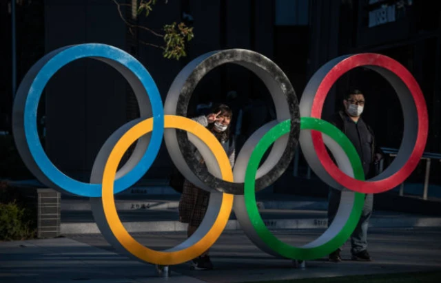 Two people pictured by the Olympics rings in Tokyo during the coronavirus pandemic