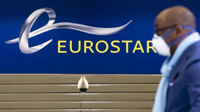 A man wears a mask in front of a Eurostar sign