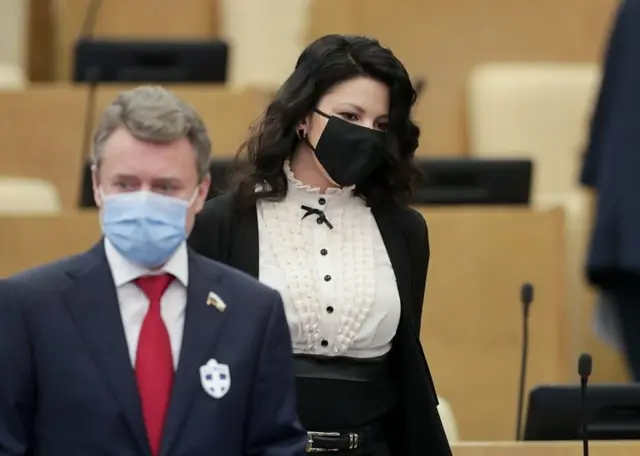 Two Russian MPs wearing coronavirus face masks, with one wearing a 'virus-stopping' badge