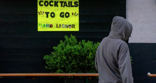 A man in a hoodie near a sign that reads: Cocktails to go hard liquor