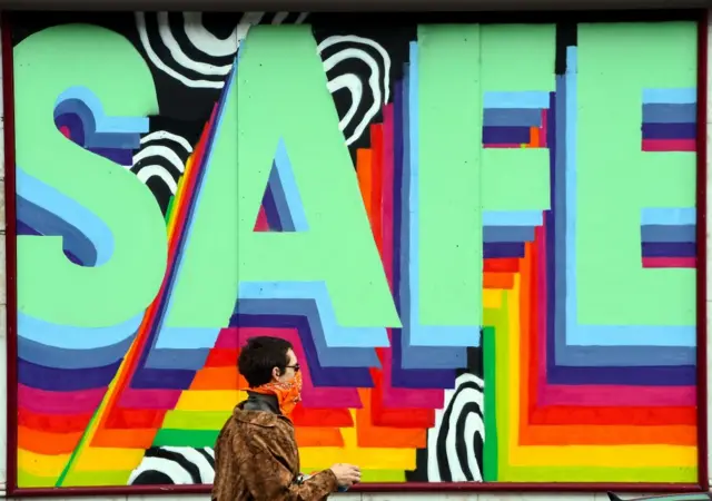 A pedestrian walks past a shuttered restaurant in Glasgow with a mural that reads "Stay Safe"