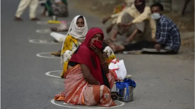 Indians wait in a line while sitting in circles marked for social distancing.