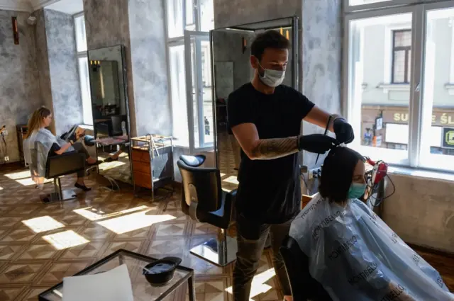 Hairdresser wearing a face mask and gloves cuts a woman's hair in Poland