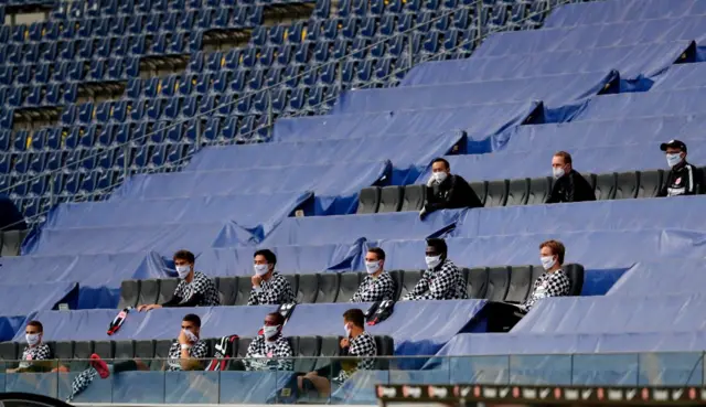 Eintracht Frankfurt's team members, keeping a distance, sit in the stands