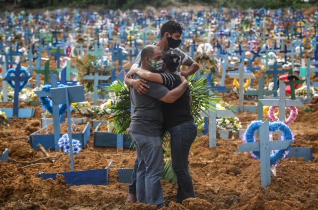 Relatives in protective masks mourn during a mass burial of coronavirus victims at the Parque Taruma cemetery in Manaus, Brazil