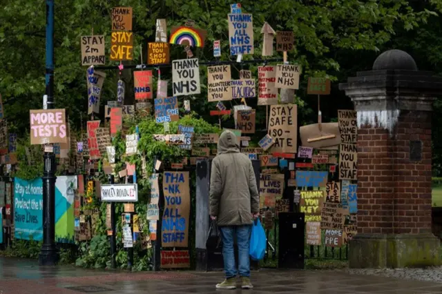 A pedestrian looks at assorted signs thanking the NHS mounted on a street corner