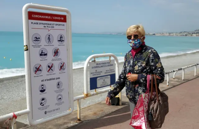 A woman walks along a beach in Nice wearing a face mask