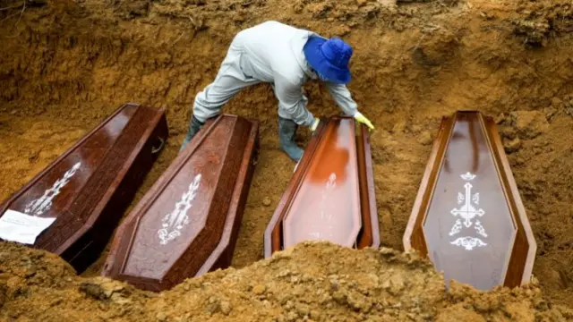 Grave digger with four coffins in a mass grave