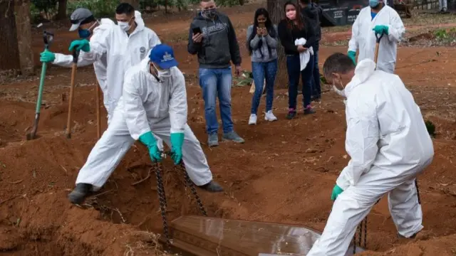 Officials wearing protective gear bury a coffin in Brazil