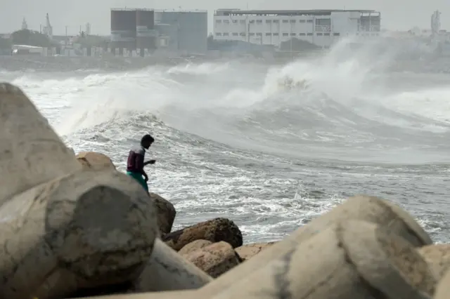 A man looks out as waves hit a breakwater at Kasimedu fishing harbour in Chennai on May 19, 2020, as Cyclone Amphan barrels towards India's eastern coast