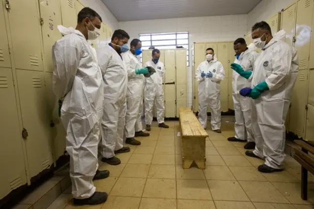 Workers wearing protective gear pray before a day of work at Vila Formosa Cemetery in Brazil