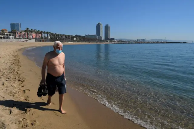 A man wearing a face mask walks at Barceloneta beach in Barcelona on 20 May, 2020 during the hours reserved for the elderly