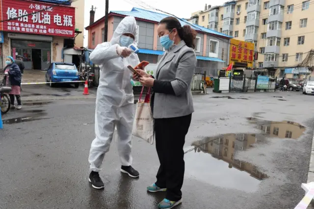 A worker in protective suit checks temperature of a woman in Jilin province, China. Photo: 17 May 2020