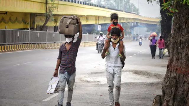 Two men walk on a road carrying a child and luggage