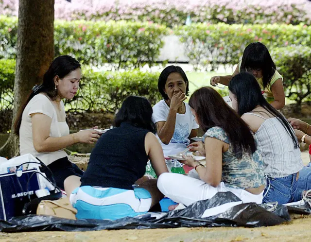 Domestic helpers enjoy a picnic in the shade at "Gulung-gulung" park in Singapore, 27 July 2003