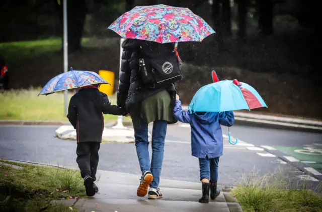 Carrying umbrellas, a mother walks her two children to school in Bondi, Sydney