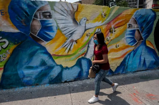 A woman wearing a face mask walks past a coronavirus-inspired mural in Mexico City