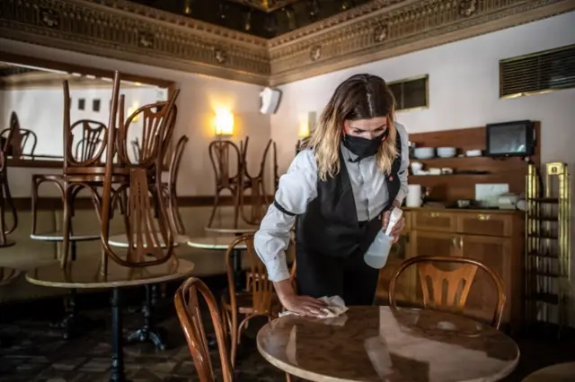 A waitress cleans tables at a cafe in Prague as it prepares to reopen