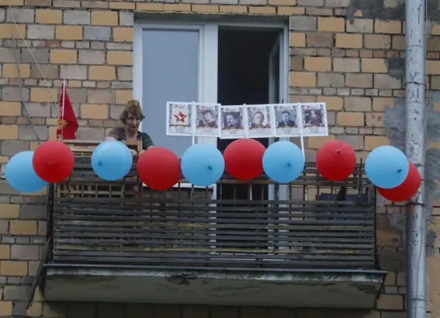 A Russian woman waves on the balcony during a moment of silence with pictures of their relatives who attended WWII in Moscow, Russia, 9 May