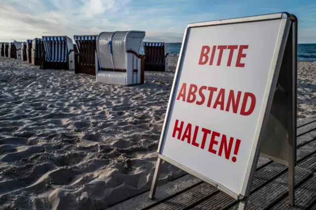 A sign reading "Please keep your distance" stands next to wicker beach chairs on a beach in N Germany