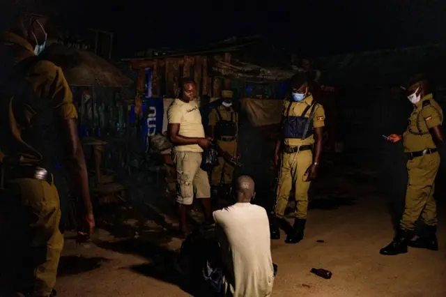 Uganda police officers question a man as they patrol on a street during the curfew after 7pm in Kampala, Uganda