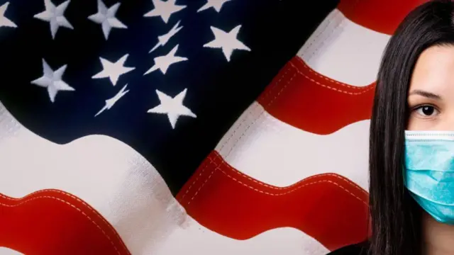 Woman in mask stands in front of an American flag