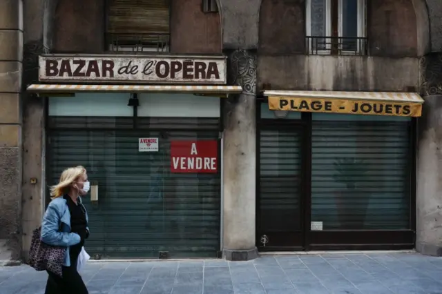 A woman walks past a closed shop with a "for sale" sign in the French Riviera city of Nice